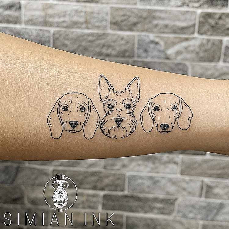 Tatuaje de tres retratos de perros en línea fina sobre el antebrazo