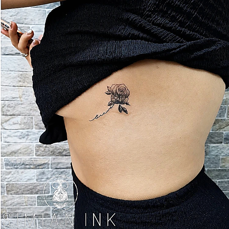 Tatuaje diminuto de una rosa con lettering fino en la costilla